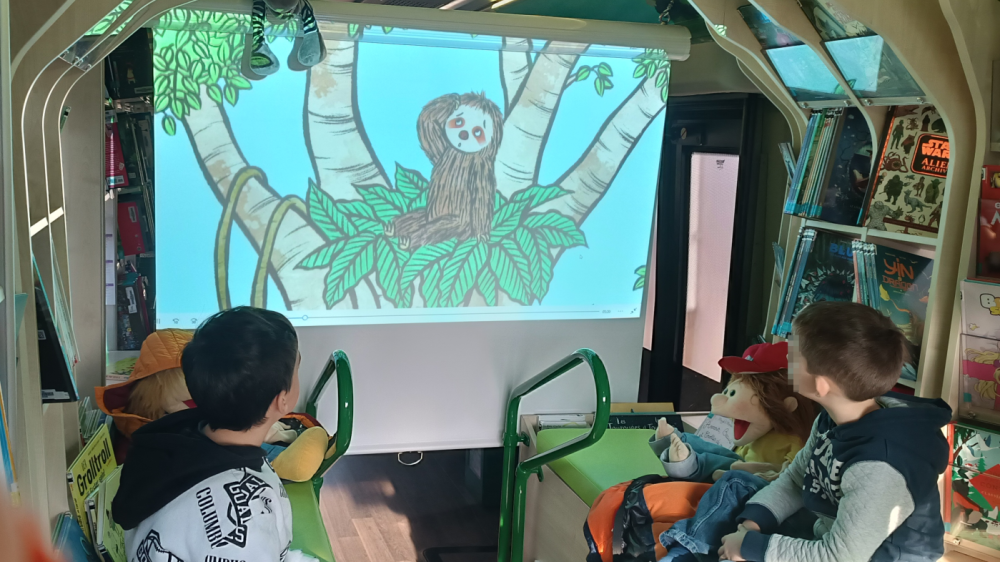 Bildporjektion eines gezeichneten Affen im BI-BUS der Stadtbibliothek, die sich Kinder anschauen Bildporjektion eines gezeichneten Affen im BI-BUS der Stadtbibliothek, die sich Kinder anschauen